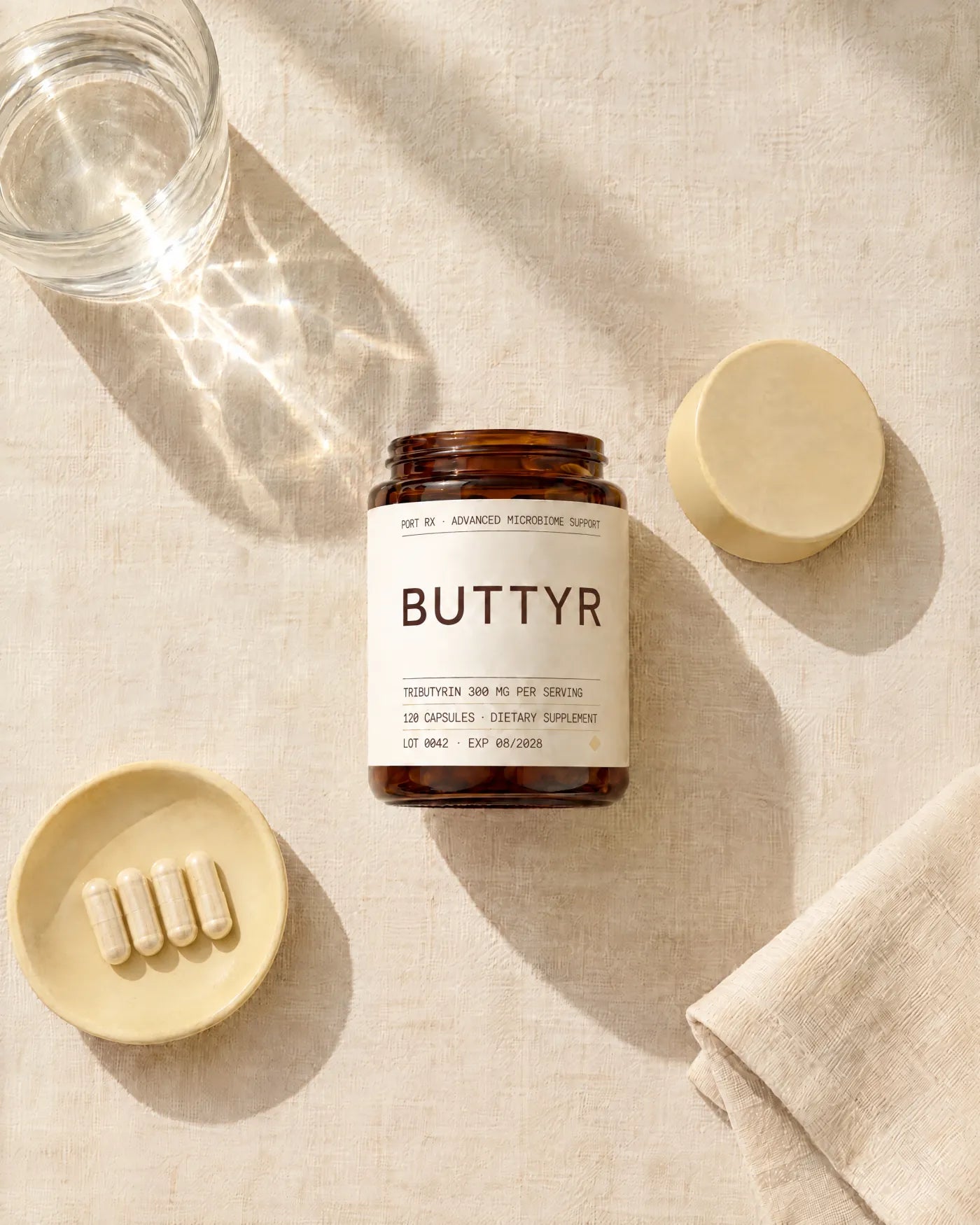 The BUTTYR jar on linen beside a dish of four capsules and a glass of water